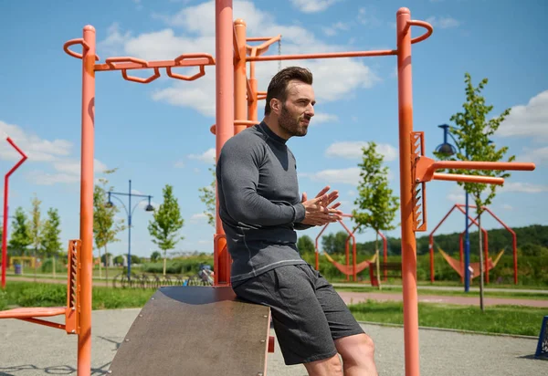 Yakışıklı maçonun kendine güvenen portresi, çekici sporcu, Avrupa 'nın beyaz kaslı spor atleti arka planda çapraz barlar ve açık hava spor sahalarında spor aletleri var.