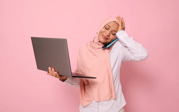マルチタスクのために彼女の頭を保持し 携帯電話で話して ノートパソコンで ヒジャーブのイスラム教徒の女性を困惑 忙しい若いアラブのビジネス女性 フリーランス 色付きの背景のオフィスワーカーの概念 — ストック写真