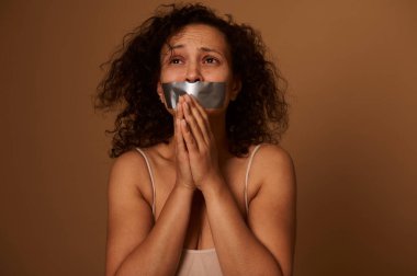 Ağzı mühürlü, korkmuş, melez bir kadının portresi yardım için yalvarıyor. Kadınlara yönelik şiddeti ortadan kaldırmak için Uluslararası Gün 'ün sosyal konsepti. Koyu arkaplan