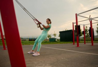 Çekici, kararlı, karışık ırk kadınlarından oluşan kolları stabil fitness kayışlarıyla dışarıda eğiten, şınav çeken, üst gövdesini, göğsünü, omuzlarını, göğüs kaslarını, göğüs kaslarını, trisepslerini çalıştıran bir kadın.