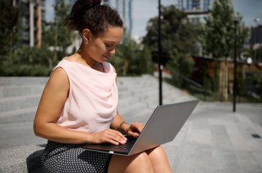 Orta yaşlı Afro-Amerikalı iş kadını merdivenlerde oturmuş, arka planda dizüstü bilgisayarla çalışıyor.