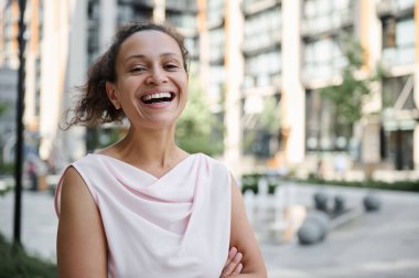 Çekici melez Latin kökenli, Afro-Amerikan kadın gülümseyen dişlek tebessümle şehir binalarının arkasında duruyor. Güzel bir iş kadınının kendinden emin portresi.