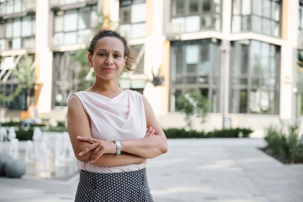 Başarılı bir orta yaşlı iş kadınının kendinden emin portresi. Yüksek binaların arka planında çapraz koçlarla kameraya poz veriyor. Şehir arkaplanı
