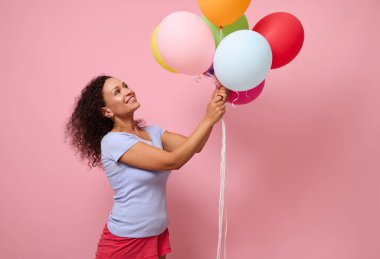 Mavi tişörtlü güzel kıvırcık saçlı bir kadın pembe renkli arka planda duruyor, ellerinde renkli parlak hava balonlarına gülümsüyor. Reklam için alanı olan yıldönümü kavramı