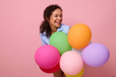 Afrika kökenli, neşeli, melez bir kadının, renkli renkli balonlarla yan yana gülen, pembe arka planda fotokopi uzayıyla izole edilmiş sevimli portresi..