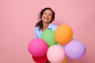 Çok renkli balonları olan neşeli, melez Latin Amerikalı bir kadının yakın plan portresi. Kameraya bakıp gülüyor. Pembe arka planda fotokopi uzayı ile izole edilmiş..