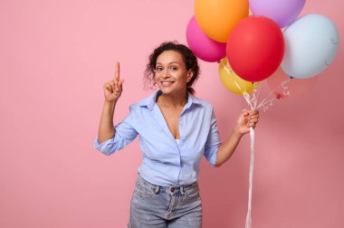 Güzel, sevimli, sevimli, neşeli, melez bir kadının beline kadar uzanan portresi. Elinde hava balonları tutan güzel bir kadın. Parlak pembe arka planda işaret parmağıyla fotokopi çeken bir kadın.
