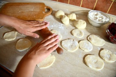 Mutfak tezgahında yuvarlak hamur kalıpları yapmak için hamuru yuvarlayan kadın aşçı ellerinin üst görüntüsü. Hamur köftelerinin yavaş yavaş pişirilmesi.