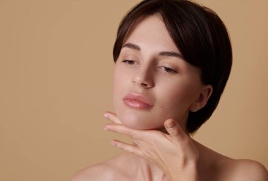 Yaşlanma karşıtı yüz ve boyun masajı yapan çekici bir Avrupalı kadının bej renkli arka planında yakın plan güzellik portresi. Deri ve vücut bakımı, refah ve refah konsepti, reklam için yer kopyalama