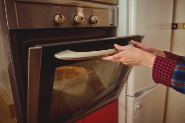 Eller sıcak bir mutfakta paslanmaz çelik fırını açmak için uzanır, ekose kollar, yemek hazırlar. Samimi, her gün evde pişirme anı..
