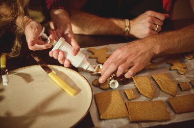 Ellerinin kurabiyelere krema sürdüğü ve parşömen üzerinde zencefilli ekmek parçaları şekillendirdiği sıcak bir mutfak sahnesi, neşeli, ev yapımı bir anı paylaşıyor..