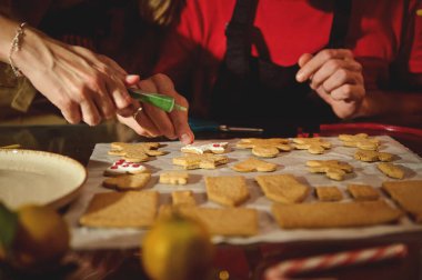 Sıcak mutfak sahnesinde, parşömen kaplı bir tepside, krema ve şekerle süslenmiş kurabiyeler, aile veya arkadaşların birlikte yemek pişirdiğini gösteriyor..
