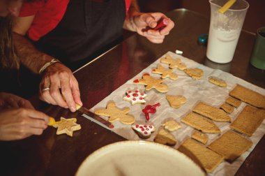 Birkaç kişi krema ve malzemeler kullanarak parşömen üzerine zencefilli kurabiye süsler. Sıcak, şenlikli bir mutfak ortamında paylaşım ve yaratıcılık..