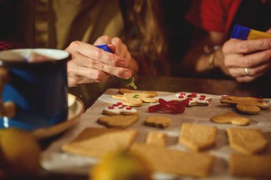 İnsanlar kalp şeklindeki kurabiyeleri kağıt kaplı bir masaya krema ve şekerle süsler, sıcak bir tatil sahnesi.