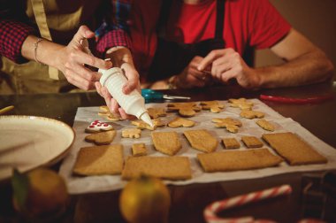 İki kişi parşömen üzerindeki kurabiyeleri kremayla süsler, aile, Noel, tatlı ve ev yapımı temalar için sıcak, şenlikli bir his verir..