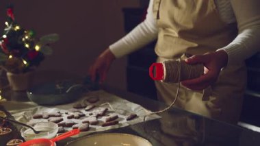 Önlüklü bir kişi, Noel kurabiyelerini toz şekere bulayıp, bayram süsü ya da tatlı hediyelere hazırlamak için dikkatlice iplere dizer..