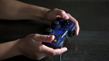 Yakın çekim, mavi bir video oyun kumandasını ustalıkla kullanan elleri yakalar. Aydınlatılmış düğmeler oyun deneyimine katkı sağlıyor. Eğlence ve modern eğlence için mükemmel bir tema..