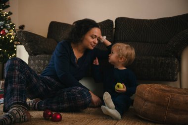 Sevgi dolu bir anne ve bebek, Noel ağacının yakınındaki sıcak bir oturma odasında, sıcaklıkla dolu, samimi bir anı paylaşırlar..