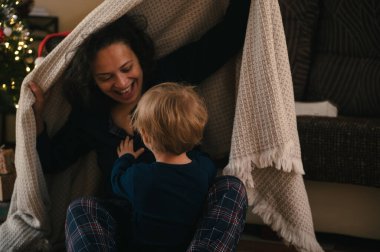 Bir anne ve çocuğun, yumuşak bir Noel ağacının yanında, yumuşak bir battaniyenin altında oynadığı sıcak, samimi bir an..