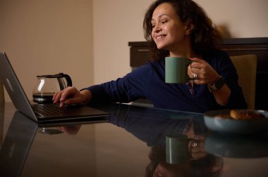 Bir kadın elinde bir kupayla cam bir masada oturuyor ve gülümsüyor. Yakınlarda bir kase yemek bulunan samimi ofis sahnesi, odak ve rahatlığı yansıtıyor..