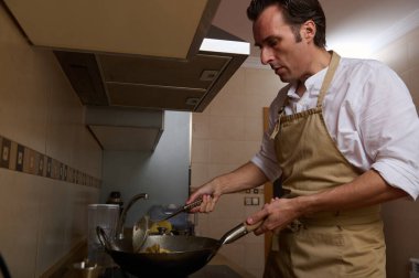 Sadık bir baba bir önlük giyer ve bir ev mutfağında yemek pişirirken, çocuğu da tavada kızartma pişirir, sıcaklığı, ilgiyi ve aile anlarını yakalar..