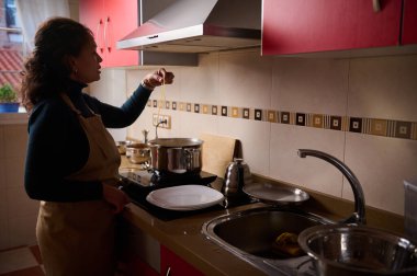 Önlüklü bir kadın, parlak bir mutfakta fırında makarna pişiriyor, erişteyi kaldırıyor. Sıcak, ev yapımı günlük yemek sahnesi.