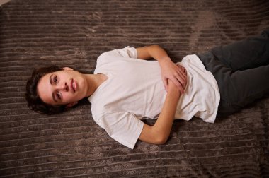 Genç bir çocuk, beyaz tişört ve koyu renk pantolon giyerek dokulu kahverengi bir halıda dinleniyor. Sakin, içe dönük ruh hali günlük Z jenerasyonunu ve günlük gençlik modunu yakalıyor..