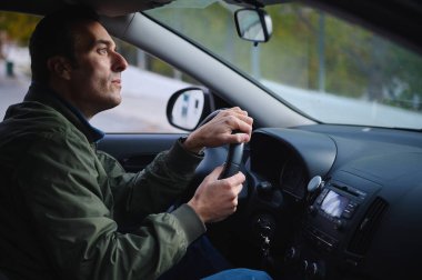 Bir adam direksiyona tutunurken konsantrasyonunu kaybeder, gösterge paneli ve yan aynayla görünür, odaklanma, güvenlik ve günlük seyahat.