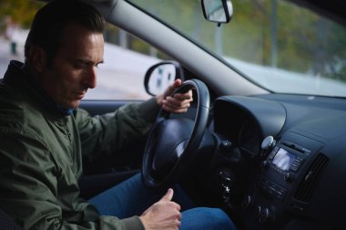 Bir adam sakin ve odaklanmış bir ifadeyle direksiyonda oturuyor. Arabanın içi ve gösterge paneli kentsel sürüş ve konsantrasyon hissi yaratıyor..