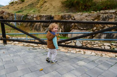 Aydınlık bir sonbahar gününde kırsal bir ahşap çitin yanında asfalt bir yolda yürüyen bir çocuk, gülümsüyor ve açık havada keşiften zevk alıyor..