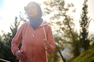 Müslüman bir Arap kadın tesettür ve pembe kapüşonlu bir kadın güneşli bir parkta koşuyor, Avrupa 'daki güncel yaşamı ve inanç, fitness ve bağımsızlık arasındaki dengeyi gösteriyor..
