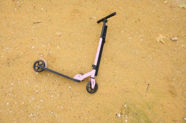 Pastel pembe bir scooter kumlu zeminde dinleniyor, açık hava eğlencesi ve macera anı yakalıyor. Boş zaman, gençlik, seyahat ve kaygısız anlar için idealdir..