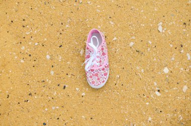 Tek bir pembe çiçekli spor ayakkabı altın kumlu zemine dayanır, gündelik yaz tarzını çağrıştırır, açık hava eğlencesi, ve eğlenceli moda.