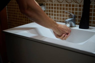 Modern bir lavaboda ellerini yıkayan bir adamın yakın çekimi, hijyen ve günlük ev rutinlerini ön plana çıkarıyor. Günlük yaşamda temiz yaşam ve kişisel bakım vurgulanıyor.