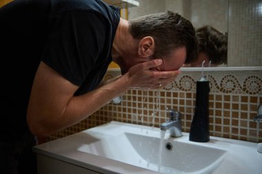 Bir adam banyo lavabosunda yüzünü yıkar, sakin bir sabah rutinini ve ev ortamında kişisel bakım anlarını yakalar..