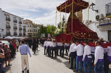 Quesada, Endülüs, İspanya. 18 Nisan 2024. Kalabalık, yerel dini bir tören sırasında altın yaldızlı bir bordo kadife tepe örtüsü taşıyan bir grup olarak caddede kuyruk oluşturuyor..