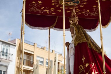 Quesada, Endülüs, İspanya. 18 Nisan 2024. Bir Bakire Meryem heykeli, altın işlemeli kırmızı kadife bir kubbe altında, dini bir tören ve gündüz kalabalığı arasında taşınır..