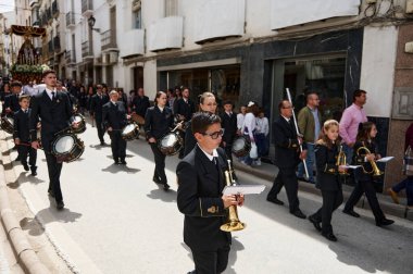 Quesada, Endülüs, İspanya. 18 Nisan 2024. Resmi bir yürüyüş bandosu, davulcuların, pirinç oyuncuların ve izleyicilerin izlediği bir sokak geçidini yönetiyor..