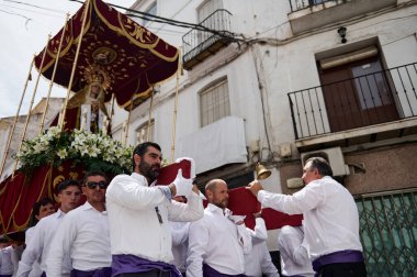 Quesada, Endülüs, İspanya. 18 Nisan 2024. Dar sokaklarda, beyaz gömlekli ve mor kuşaklı adamların kadife bir gölgeliğin altında heykel taşıdığı dini bir geçit töreni..