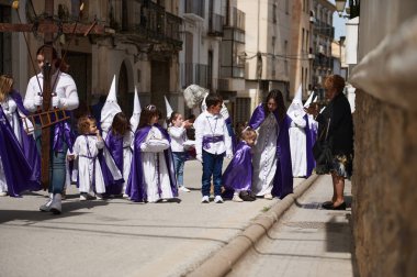 Quesada, Endülüs, İspanya. 18 Nisan 2024. Beyaz ve mor cüppeli çocuklardan oluşan bir sokak geçit töreni. Yetişkinlerle birlikte, dini bir tören alayı atmosferi yakalıyorlar..