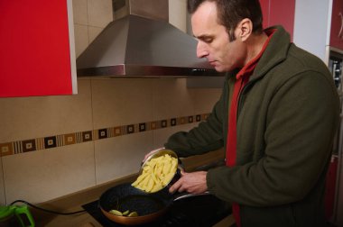 Bir adam, ev mutfağındaki bir ocağın tepsisine dilimlenmiş patatesleri döker ve her gün samimi bir yemek anı yakalar..