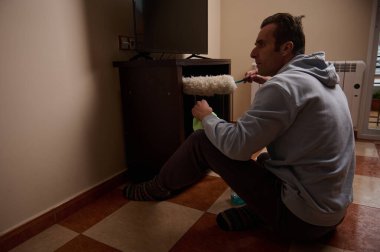 Gri kapüşonlu bir adam yerde oturur, rahat bir evde ahşap bir dolabı silindirle boyar. Sıradan, odaklanmış ve düzenli, iş yerinde ev gelişimini kaydediyor..