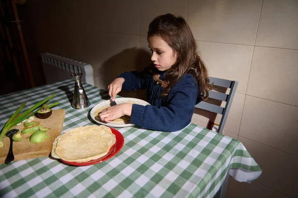 Avokado ve zeytinyağlı yassı ekmeklerle beslenen şirin bir çocuk yeşil kareli masa örtüsüyle kaplı bir yemek masasında oturuyor. Vejetaryen ve vejetaryen diyet kavramı. Sağlıklı beslenme