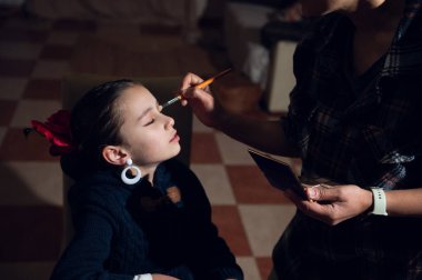 Bir yetişkin fırçayla makyaj yaparken genç bir kız gözleri kapalı oturur. Sıcak bir evde sıcak bir bakım ve bağ anı..