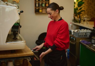 Kırmızı kazaklı bir İspanyol kafe sahibi tezgahta espresso hazırlıyor. Konukseverlik, küçük işletmeler ve rahat bir kafe atmosferi sergiliyor..