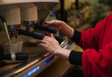 İspanyol bir kafe sahibi espresso makinesiyle ilgileniyor. Buhar yükselirken ustalıkla ateş ediyor. Sıcak, misafirperverlik, küçük işletme ve günlük kafe rutinini vurgulayan bir ortam..