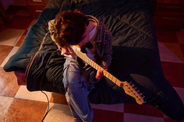 Sıcak, rahat bir ışıkta, elektro gitarını tıngırdatan bir insan. Müzik, hobi ve ev hayatı temaları için ideal.