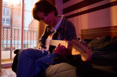 Sıradan giyimli genç bir adam yatakta oturur, güneşli bir balkon penceresinde elektro gitar çalar, yumuşak ve yaratıcı bir hava yaratır..