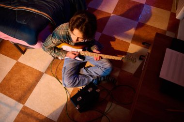 Genç bir müzisyen yerde bağdaş kurup kareli bir yatak odasındaki küçük bir amfiyle elektro gitar çalar, rahat ve yaratıcı bir ruh hali yayar..