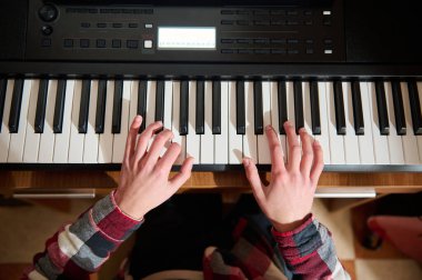 Genç bir piyanist odaklanmış elleri olan elektronik bir klavye çalar. Ekose gömlek giyen sahne, evde pratik, hobi ve müzikal yaratıcılığı yakalıyor..